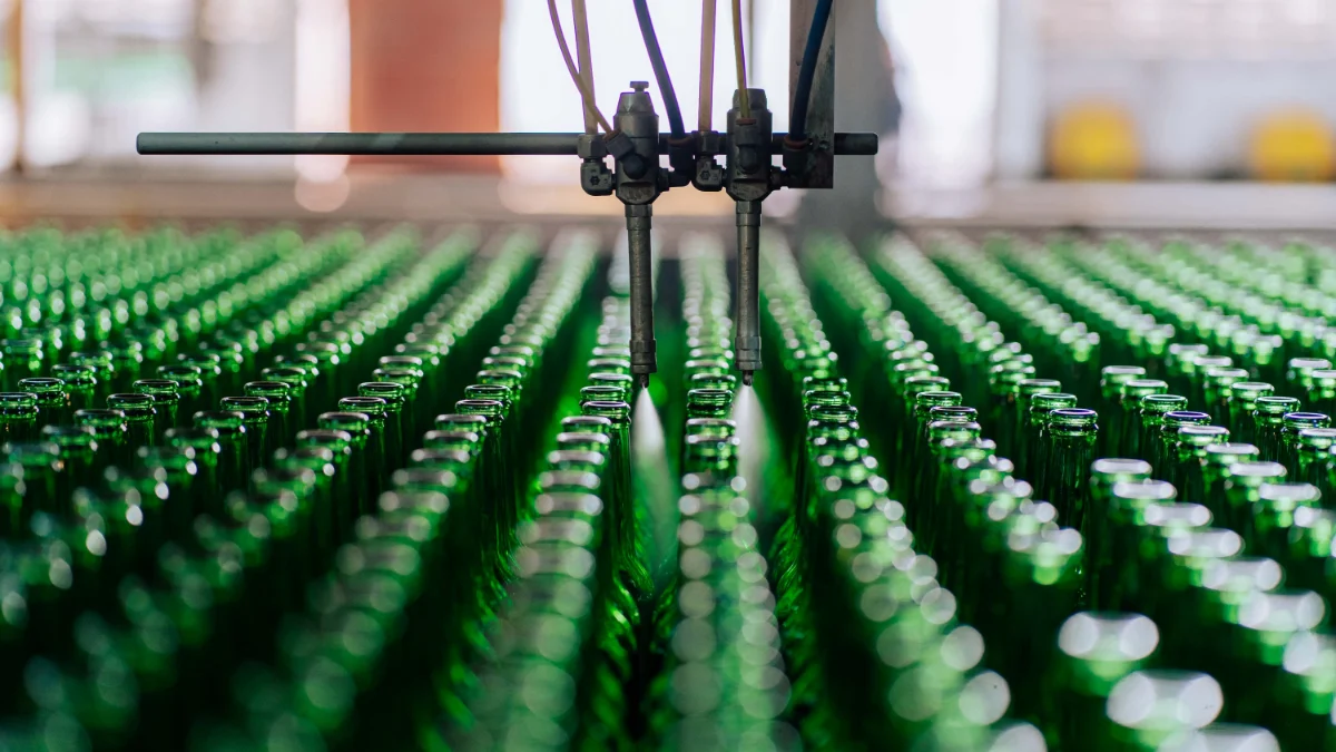 Na zdjęciu widoczna jest zautomatyzowana linia produkcyjna, na której szklane butelki są produkowane w przemysłowym procesie