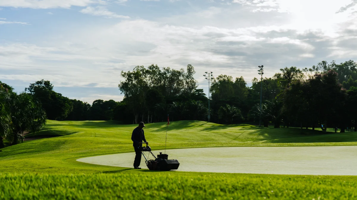 Ogrodnik koszący zieleń na polu golfowym w słoneczny dzień, prezentujący bujne krajobrazy i utrzymanie