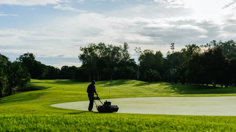 Ogrodnik koszący zieleń na polu golfowym w słoneczny dzień, prezentujący bujne krajobrazy i utrzymanie