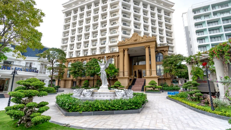Eleganckie wejście do hotelu z dopracowanymi rzeźbami i bujnym zagospodarowaniem ogrodu, co wskazuje na profesjonalne zarządzanie hotelowym